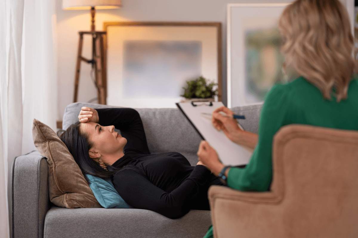 Client lying on a sofa while a therapist takes notes